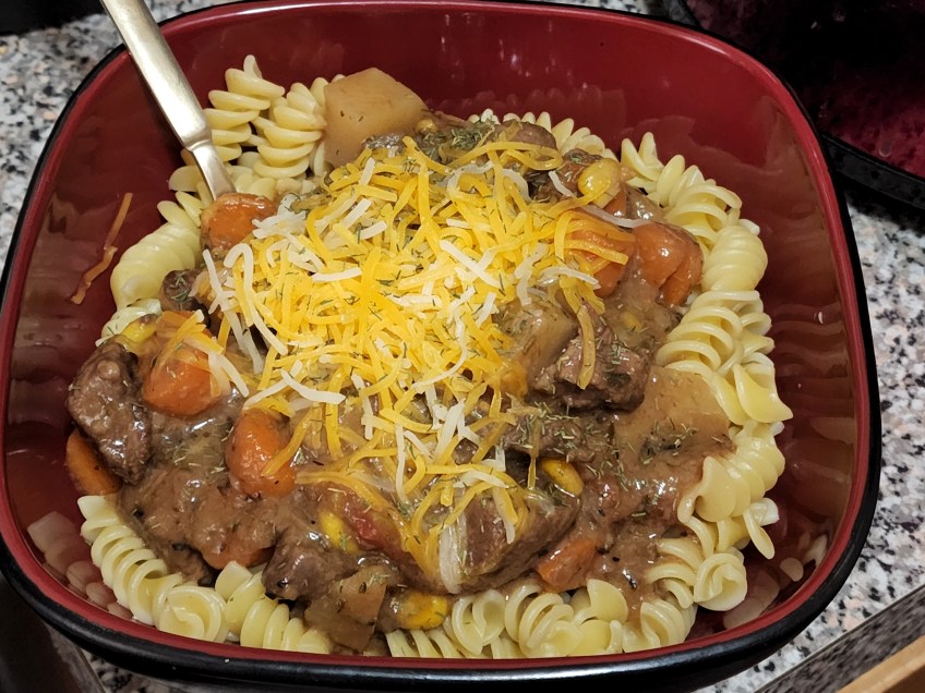 Bowl of beef stew served over pasta, topped with cheese. blend.