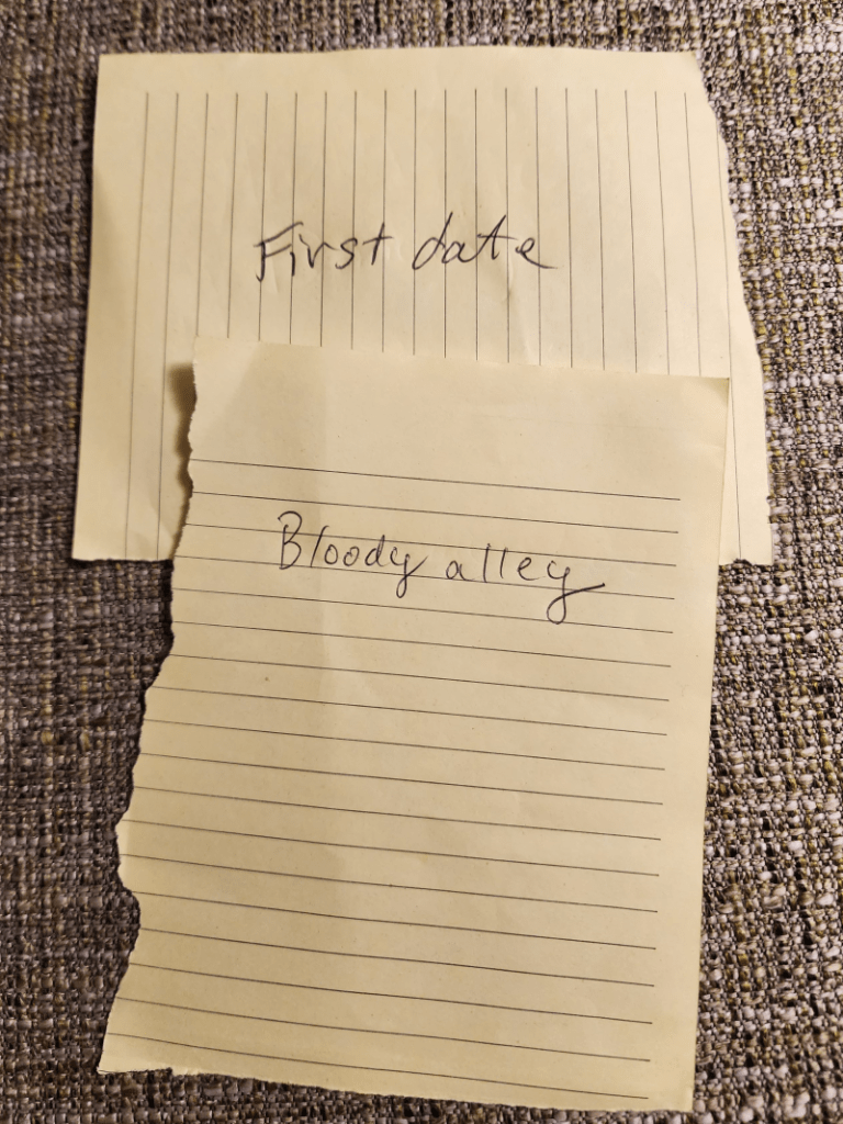 Two ripped papers with writing prompts. top one: First date. Second one: Bloody alley