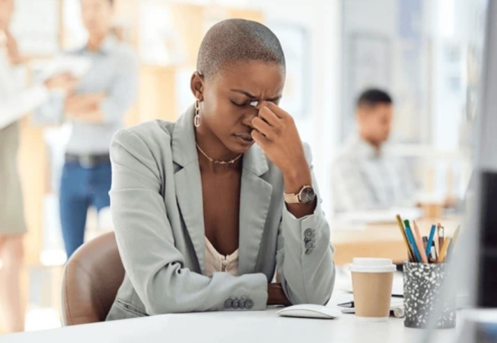 Woman sitting at office desk pinching bridge of her nose in stress